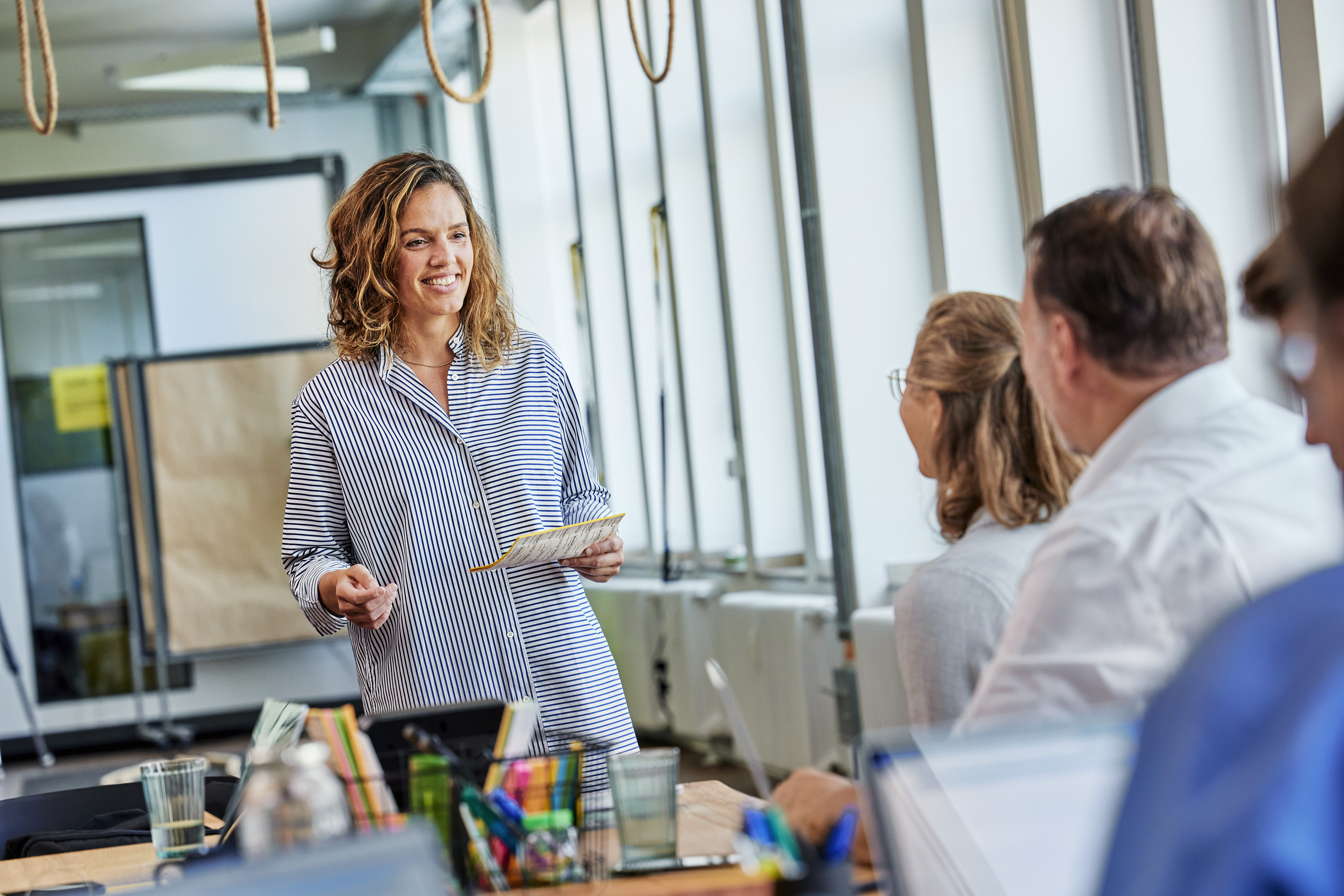 Eine Mitarbeiterin hält eine Präsentation und lächelt dabei. Sie wirkt selbstbewusst und engagiert, während sie ihre Botschaft mit Begeisterung vermittelt.