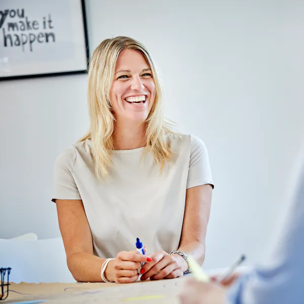 Mitarbeiterin der Allfoye Managementberatung sitzt lächelnd an einem Tisch