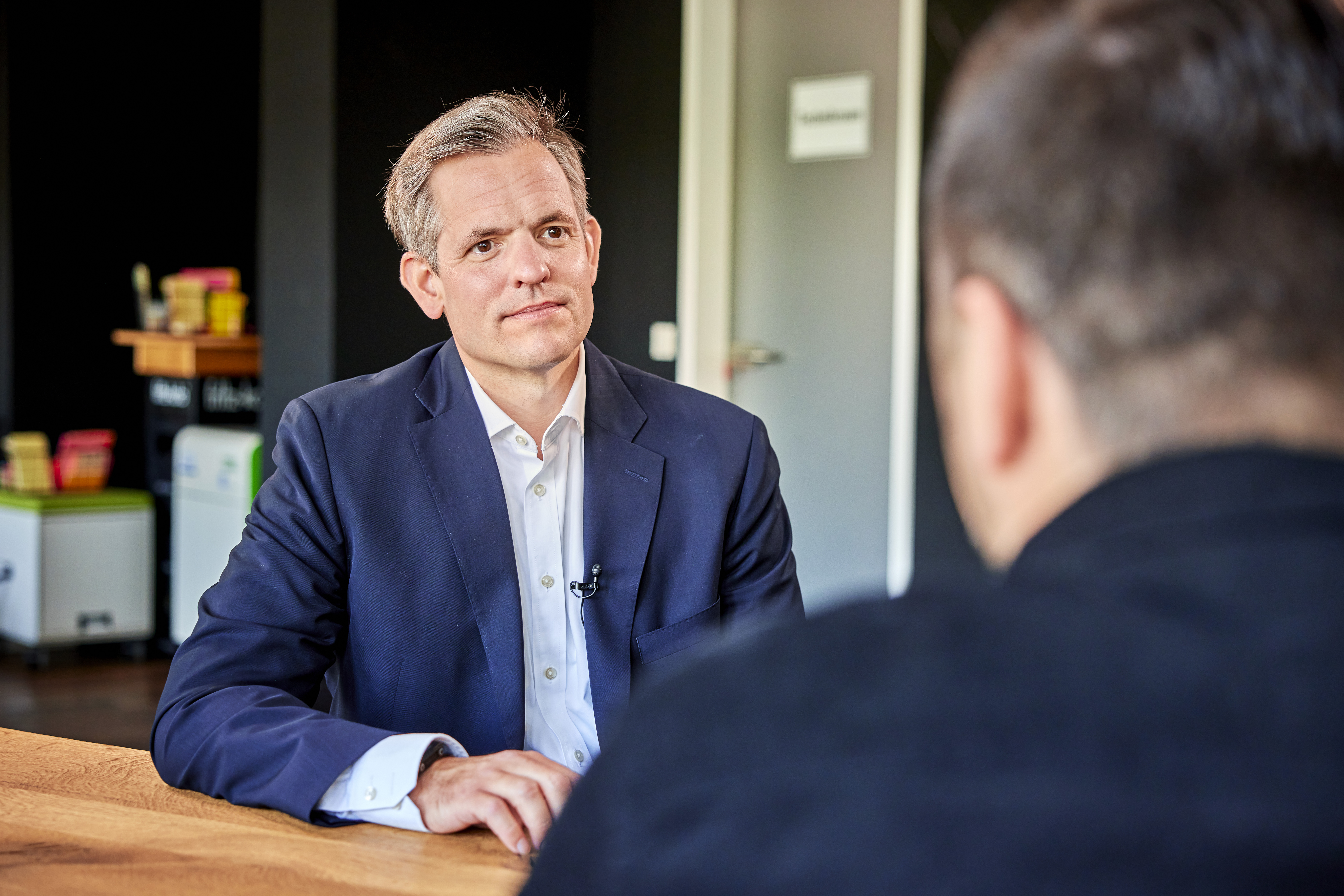 Geschäftsführer der Allfoye Managementberatung, trägt einen dunkel blauen Anzug und sitzt an einem Tisch 