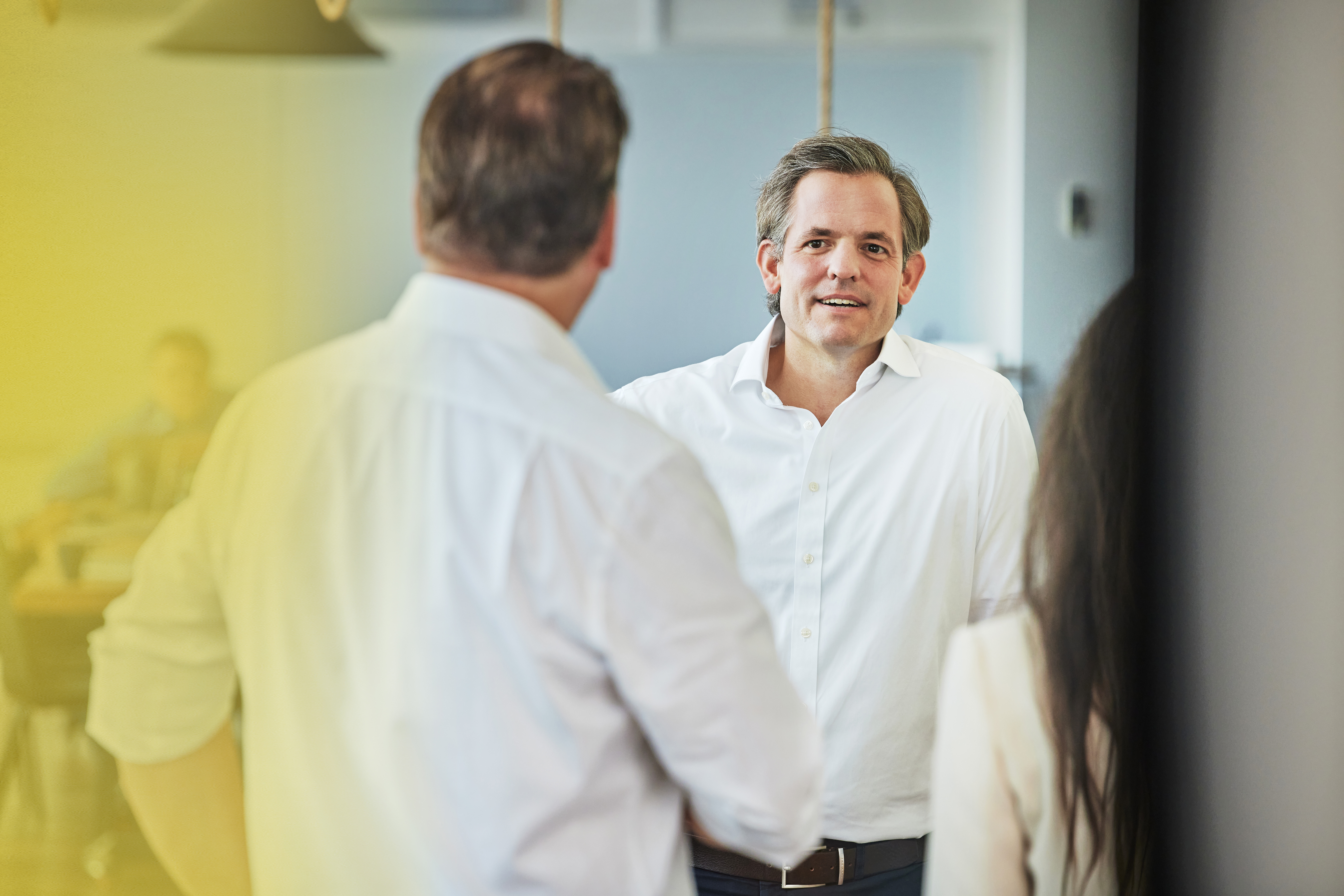 Der CEO unterhält sich mit einem Mitarbeiter in einem kreativ gestalteten Raum. Beide stehen einander zugewandt und wirken fröhlich, was auf eine offene und positive Arbeitsatmosphäre hinweist.