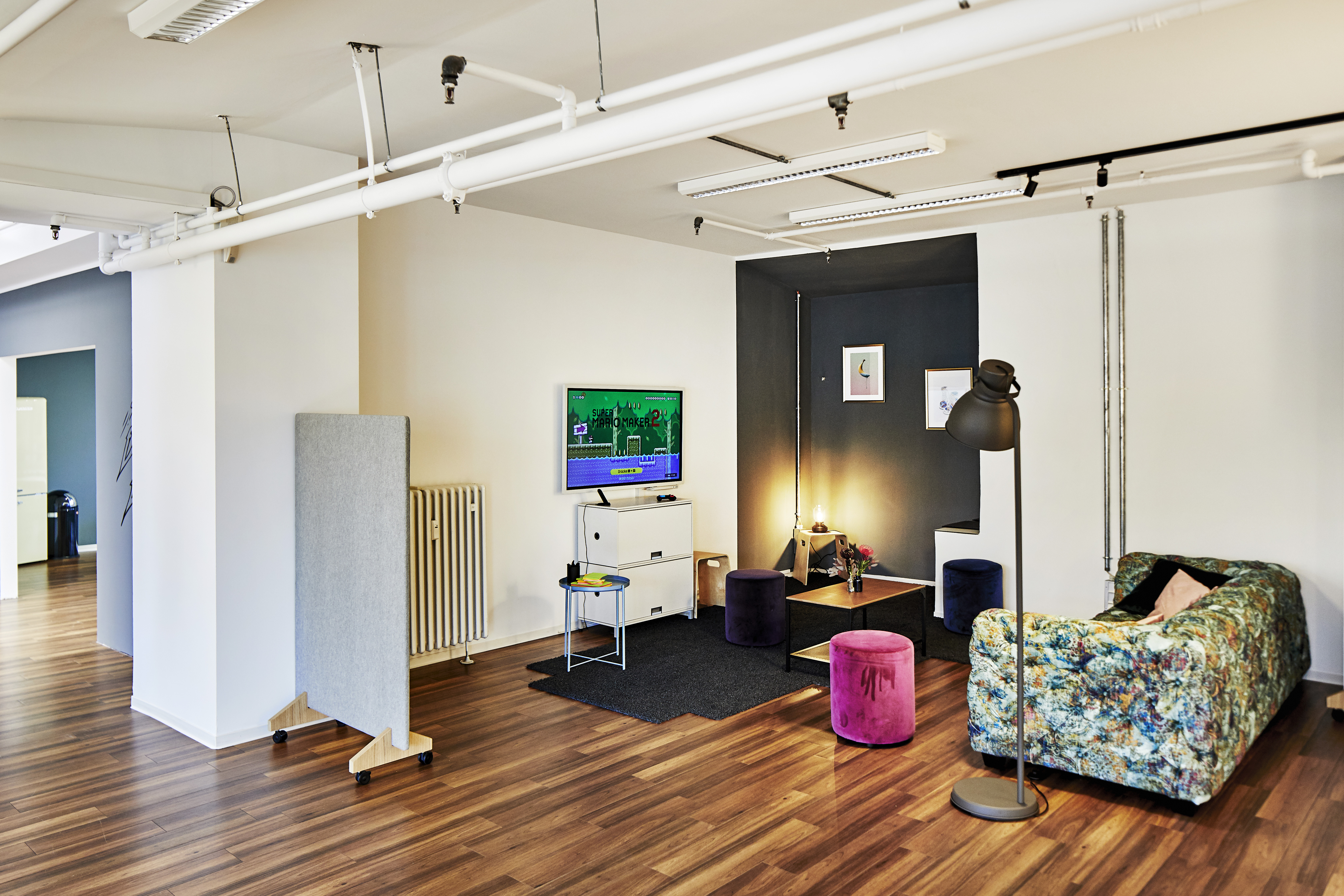 Ein offener, inspirierender Arbeitsraum mit einer stilvollen Couch und einem Fernseher für flexible Arbeits- und Besprechungsmöglichkeiten.