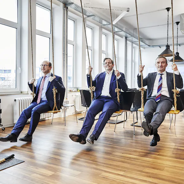 Drei Mitarbeitende sitzen auf einer Schaukel in einem innovativen Arbeitsraum.