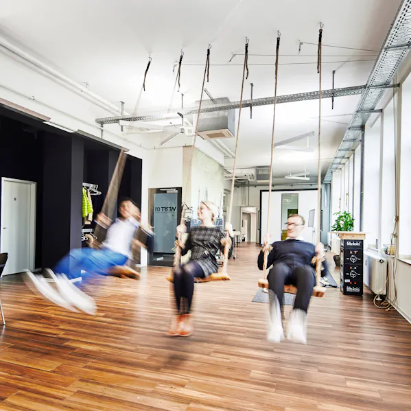 Drei Mitarbeitende sitzen auf einer Schaukel in einem innovativen Arbeitsraum.