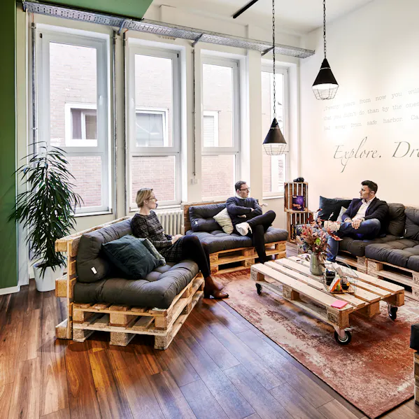 Drei Mitarbeitende sitzen in einem modernen Workspace auf einer Couch und unterhalten sich.