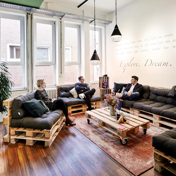 rei Mitarbeitende sitzen in einem modernen Workspace auf einer Couch und unterhalten sich.