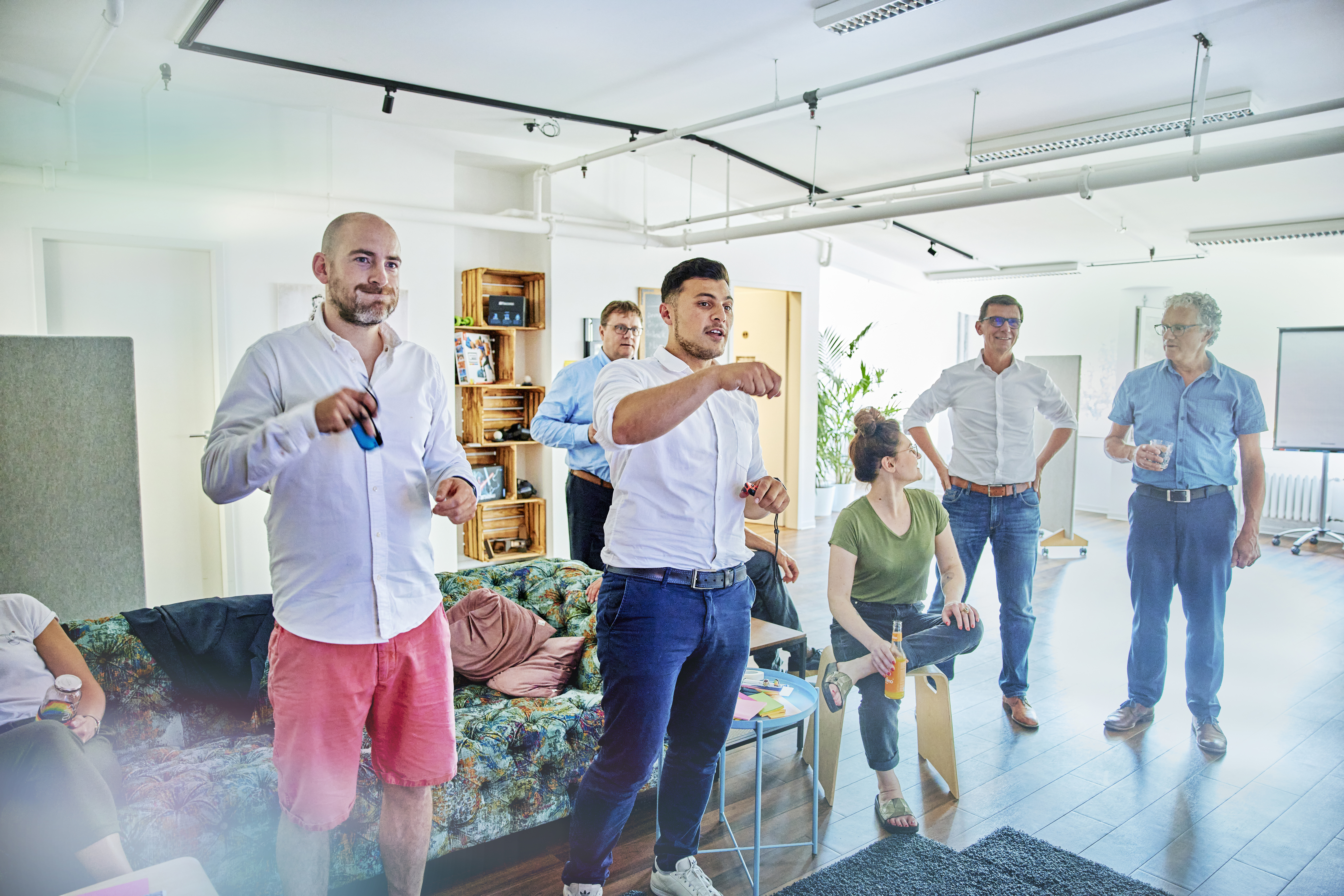 Ein Team sitzt locker zusammen und schaut zu, wie einige Mitarbeitende an einem Fernseher ein Spiel spielen.