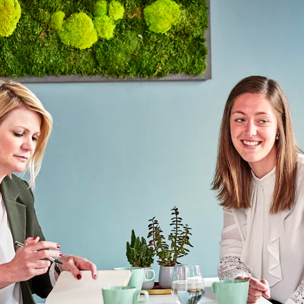 Mitarbeiterinnen der Allfoye Managementberatung sitzen an einem Tisch und lachen gemeinsam. Die Stimmung ist fröhlich und locker.