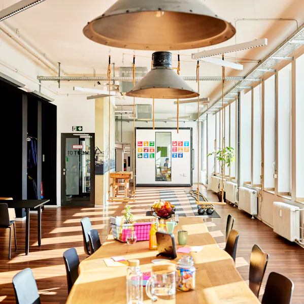 Ein innovativer Raum zum gemeinsamen Arbeiten. In der Mitte des Bildes ist ein Tisch mit Stühlen zu sehen. Die Atmosphäre ist warm, an den schwarzen Wänden sind Zeichnungen mit Kreide erkennbar.