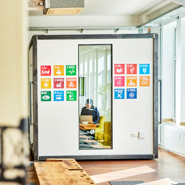 Ein inspirierender Arbeitsbereich mit einem kreativen Cube als Meetingraum. Die Wände des Cubes zeigen die 17 globalen Nachhaltigkeitsziele.