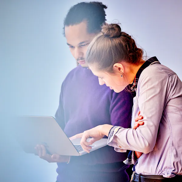 In einem lichtdurchfluteten Raum betrachten zwei Menschen aufmerksam den Bildschirm eines Laptops.