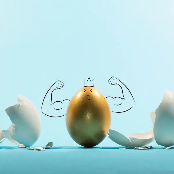 Ein goldenes Ei mit gemalten Muskeln, einer Krone und einem grinsenden Gesicht steht im Mittelpunkt vor einem blauen Hintergrund. Daneben liegen viele weiße, zerbrochene Eierschalen, die eine humorvolle und fantasievolle Szene schaffen.'